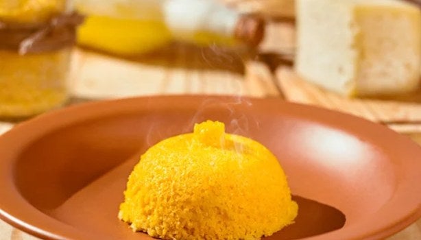  Cuscuz amarelo servido em prato de barro, ainda quente, sobre mesa rústica.