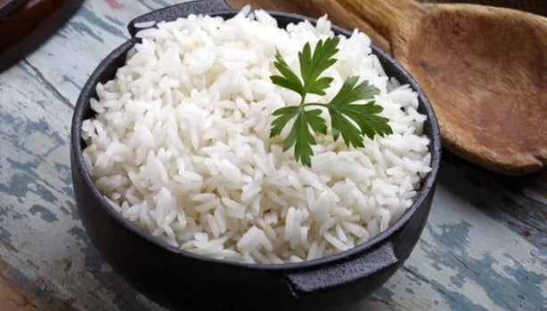 Arroz branco cozido em panela preta, finalizado com folha de salsa, sobre superfície rústica.