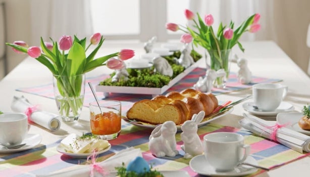 Decoração de Páscoa: Mesa decorada com pratos, talheres, pães, vaso com flores e xícaras