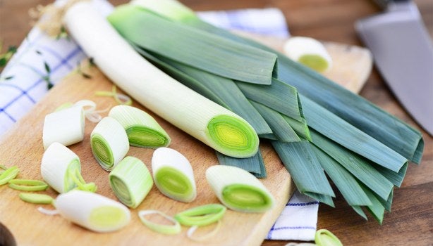 Alho-poró inteiro e fatiado sobre uma tábua de madeira, mostrando o ingrediente fresco para preparo de receitas.
