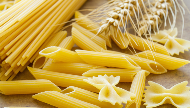 Massas secas italianas dos tipos espaguete, penne e farfalle com espigas de trigo em composição culinária.