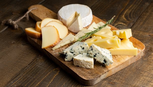 Tábua de madeira com variedade de queijos, incluindo brie, queijo azul, suíço e defumado.
