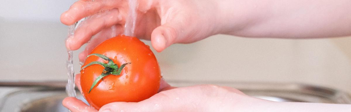 Como higienizar frutas, verduras e alimentos: uma pessoa lavando um tomate na pia