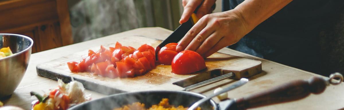 Comida italiana: uma pessoa cortando tomate em cima da tábua de madeira