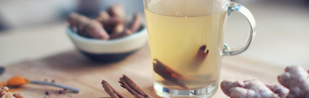 Chá de Gengibre: chá de gengibre em uma xícara, com canela dentro e em volta da xícara, em cima de uma mesa de madeira