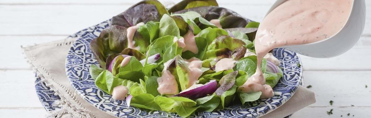 Molho rosê sendo derramado em uma salada em cima de um prato