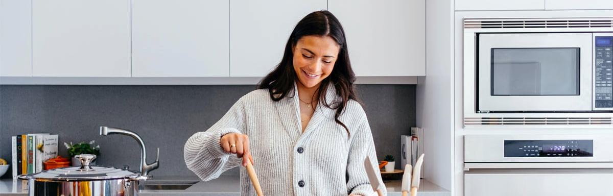 Como economizar gás de cozinha: Mulher sorrindo em uma cozinha com as mãos em uma panela 