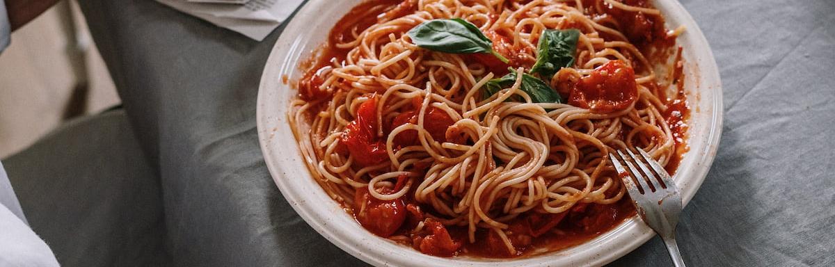 Opções de almoço rápido e fácil:Macarrão com molho de tomate no prato com um garfo ao lado em cima de uma mesa com pano cinza