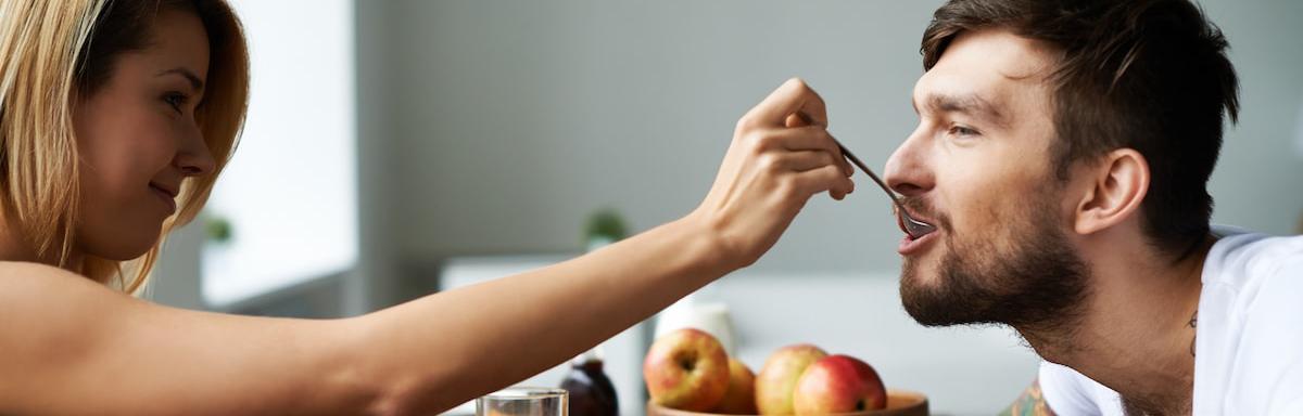 Café da Manhã Romântico: Mulher à esquerda colocando uma colher com comida na boca de um homem à direita