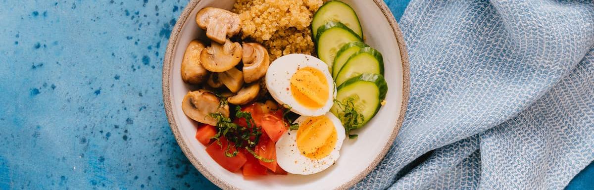 Aprenda como cozinhar ovo:  Tigela com ovo, picles, tomates, cogumelos, em cima de uma mesa azul