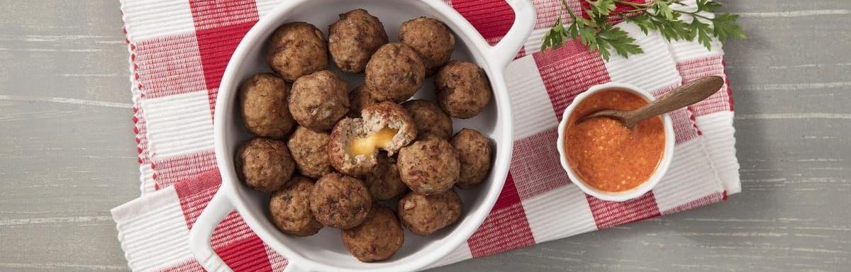 Panela com vários bolinhos de carne moída recheados com queijo. À direita um molho e, abaixo, um pano xadrez (Vermelho e bran