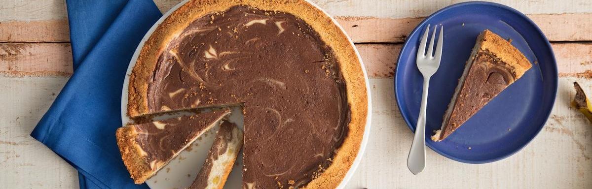 Torta de chocolate com dois pedaços cortados sobre um pano azul. À direita, pedaço de torta sobre um prato com um garfo ao la