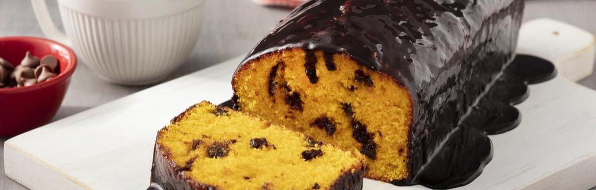 Bolo de cenoura com cobertura de chocolate em cima de um prato, à esquerda pote com gotas de chocolate