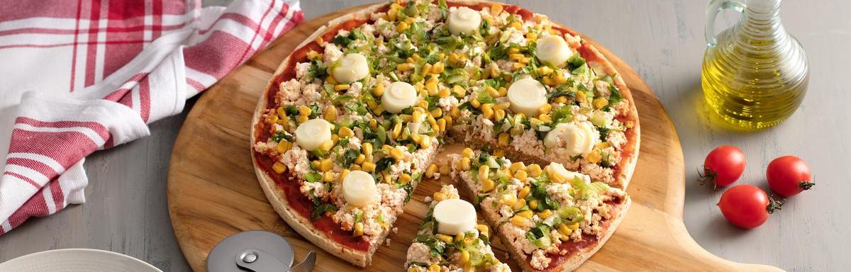 Pizza com duas fatias cortadas sobre uma tábua de madeira, abaixo da pizza tem um cortador e à direita azeite e dois tomates.