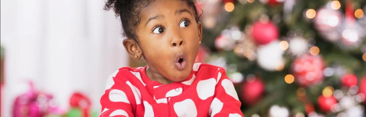 Presentes de Natal: menina negra com cara de surpresa, com a mão em um presente