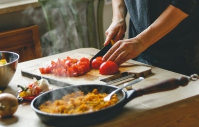Comida italiana: uma pessoa cortando tomate em cima da tábua de madeira