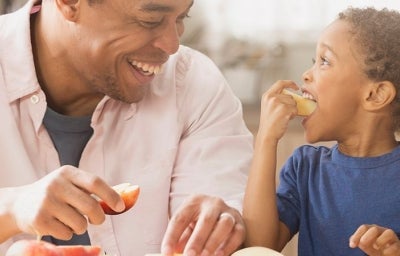 Lanche da Tarde: Um homem negro com uma maçã na mão e uma criança negra comendo uma maçã 
