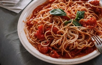 Opções de almoço rápido e fácil:Macarrão com molho de tomate no prato com um garfo ao lado em cima de uma mesa com pano cinza