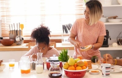 Dicas de café da manhã: Duas crianças negras à esquerda, dois adultos negros à direita, com frutas, leite, pão e café na mesa