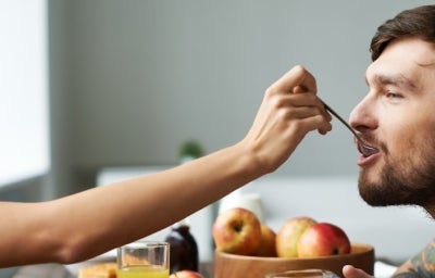 Café da Manhã Romântico: Mulher à esquerda colocando uma colher com comida na boca de um homem à direita