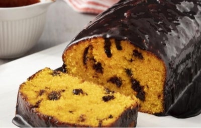 Bolo de cenoura com cobertura de chocolate em cima de um prato, à esquerda pote com gotas de chocolate