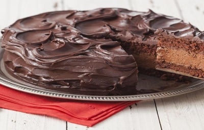 Imagem de um bolo mousse de chocolate com uma fatia sendo retirada com uma espátula mostrando o recheio.