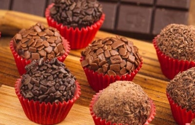 Imagem de brigadeiros gourmet com chocolate granulado em forminhas vermelhas.