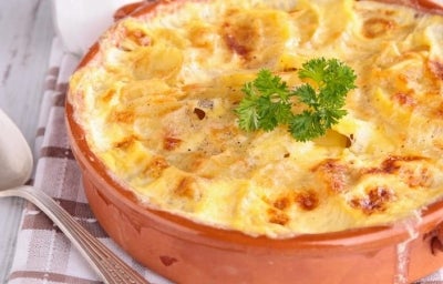 Imagem de uma travessa redonda com uma receita gratinada com queijo e uma folha de salsinha.