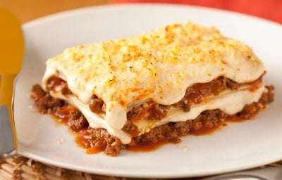 Imagem de uma fatia de lasanha a bolonhesa com molho e queijo.