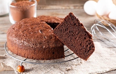 Imagem de um bolo redondo de chocolate com uma fatia em evidência.