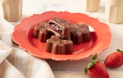 Imagem de bombons de chocolate em formato de flor com recheio de morango sobre um prato vermelho.