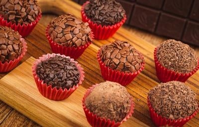 Imagem de brigadeiros de chocolate em forminhas vermelhas em uma tábua de madeira.