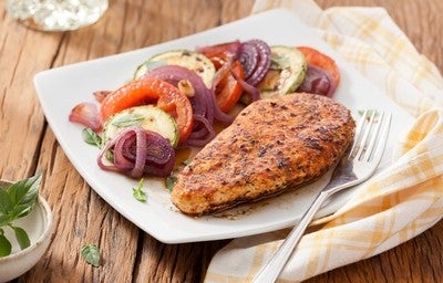 Filé de frango grelhado suculento com legumes grelhados em um prato branco.