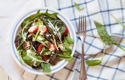 Bowl de salada verde com tomates e molho de iogurte sobre um pano xadrez branco e azul.