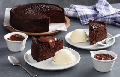 Bolo de chocolate servido com bolas de sorvete de creme e cobertura, acompanhado de pequenas tigelas com calda de chocolate.