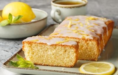 Bolo de limão com cobertura glaceada e raspas de limão, servido em fatias sobre bandeja com limão fresco ao lado.