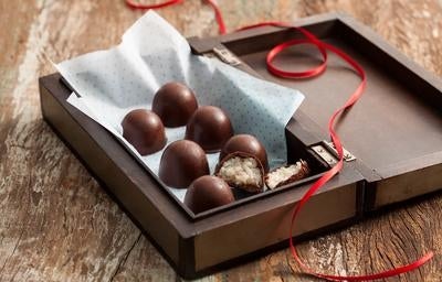 Bombons de chocolate com recheio de coco em caixa de madeira decorada com fita vermelha.