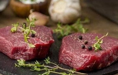 Bife cru de carne vermelha com especiarias, em cima de uma tábua preta. A imagem representa a carne magra.