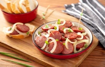 Prato de linguiça acebolada servido em tigela vermelha, acompanhado de fatias de pão ao fundo.