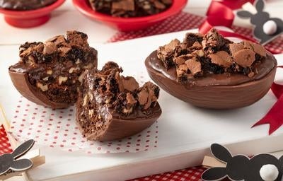 Ovo de Páscoa de chocolate recheado com brownie e pedaços crocantes decorado em uma bandeja branca.