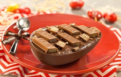 Ovo de Páscoa de chocolate ao leite decorado com pedaços de KitKat, servido em prato vermelho.