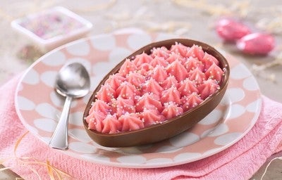 Ovo de Páscoa de chocolate ao leite recheado com Nesquik e confeitos coloridos, servido em prato decorado.
