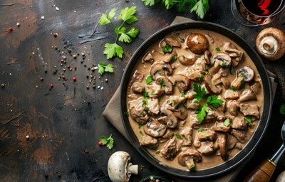 Prato de strogonoff de carne com cogumelos fatiados em molho cremoso, decorado com salsa fresca.