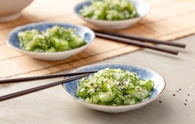 Salada sunomono de pepino japonês com gergelim servida em prato azul e branco.