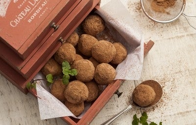 Trufas de chocolate polvilhadas com cacau em pó, servidas em caixa rústica de madeira, com toque de folhas de hortelã.