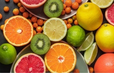 Frutas cítricas variadas como laranja, limão, kiwi e grapefruit cortadas ao meio, dispostas em fundo escuro.