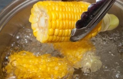 Espiga de milho sendo retirada da água fervente com pegador, mostrando o cozimento do milho.