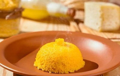  Cuscuz amarelo servido em prato de barro, ainda quente, sobre mesa rústica.