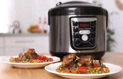 Prato com carne e legumes servido à frente de uma panela de pressão elétrica sobre a bancada.