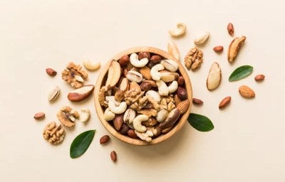 Mix de castanhas e nozes em tigela de madeira, com amêndoas, castanha-de-caju e nozes sobre fundo claro.